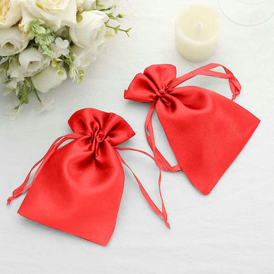 Red satin drawstring bags on a table with flowers.