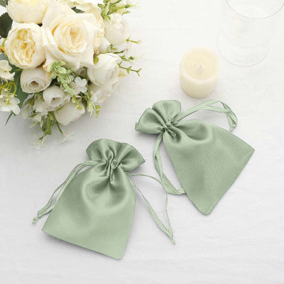 Green satin drawstring bags next to a bouquet and candle.