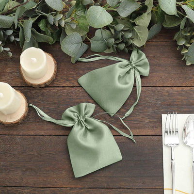 Green satin drawstring bags on a wooden table with candles and foliage.