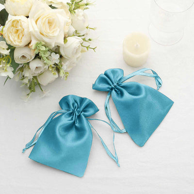 Turquoise satin favor bags with ties, styled with white flowers and a candle.