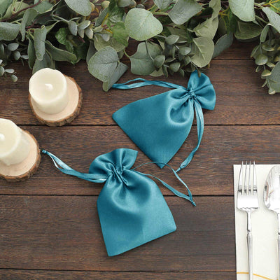 Teal satin gift bags on a wooden table with greenery and candles.