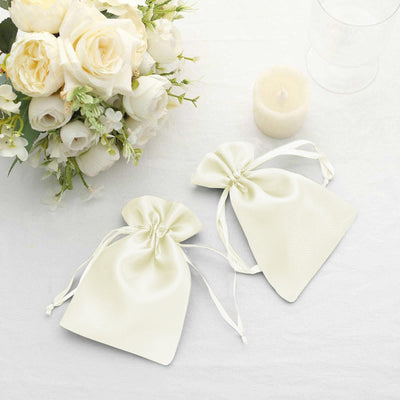 Elegant ivory satin gift bags next to a floral arrangement and candle.