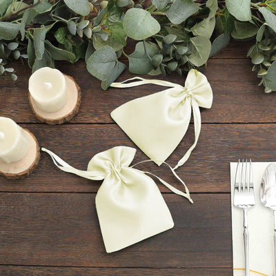 Satin gift bags in pale green, styled with candles and greenery on a wooden table.