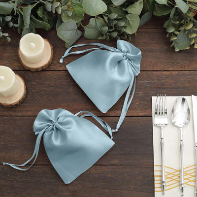 Light blue satin drawstring bags on a wooden table with candles and cutlery.