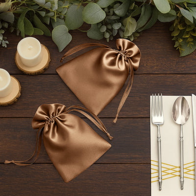 Brown satin drawstring bags on a wooden table with candles and utensils.