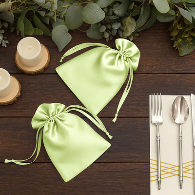 Satin green favor bags on a wooden table with candles and cutlery.
