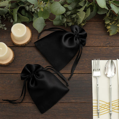 Black satin drawstring bags on a rustic wooden table with candles and utensils.