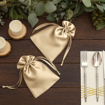 Two elegant gold satin drawstring bags on a rustic wooden table.