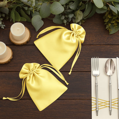Yellow satin gift bags on a rustic wooden table with candles and silverware.