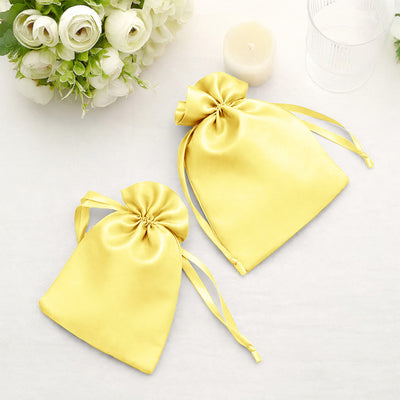 Yellow satin drawstring pouches on a table with flowers and a candle.