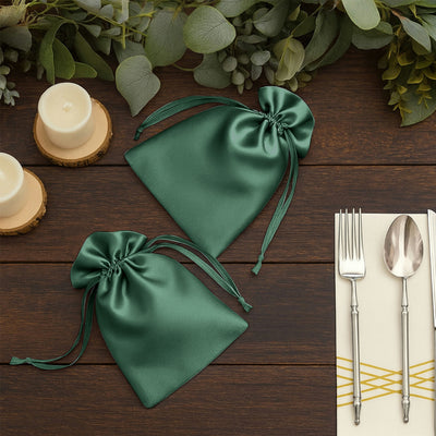 Green satin drawstring bags on a wooden table with candles and utensils.