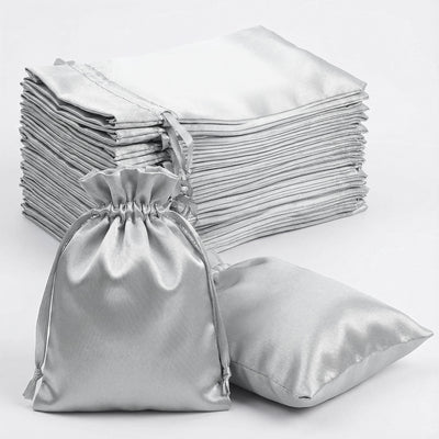 Silver satin drawstring bags and pillowcases stacked on a white background.