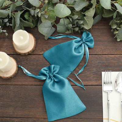 Teal satin favor bags with ribbons on a rustic table setting.