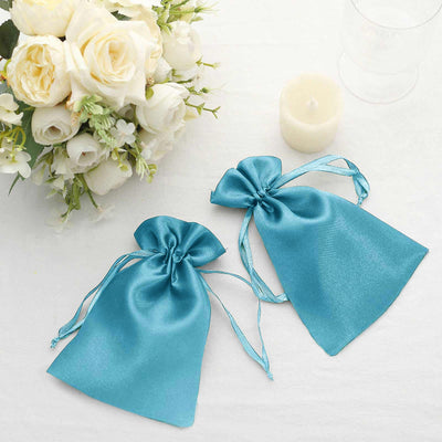 Turquoise satin gift bags with drawstrings, styled with flowers and a candle.