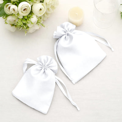 White satin drawstring bags on a table with flowers and a candle