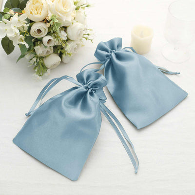Two blue satin drawstring bags on a table with floral arrangement.
