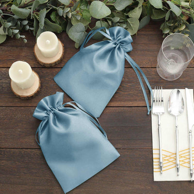 Blue satin gift bags on a rustic table with candles and dining utensils.