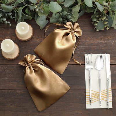 Two elegant gold satin gift bags on a wooden table with candles and cutlery.