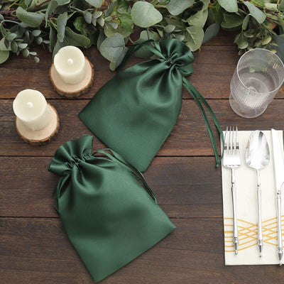 Green satin gift bags on a wooden table with candles and utensils.