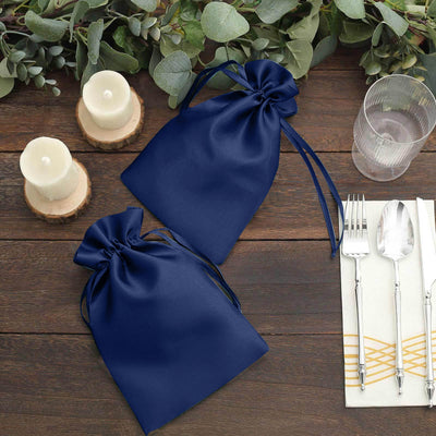 Navy satin drawstring bags on a rustic table setting with candles and utensils.