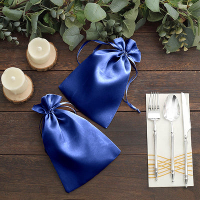 Blue satin gift bags on a wooden table with candles and cutlery.