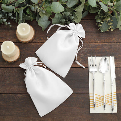 White gift bags on a rustic wooden table with candles and silverware.