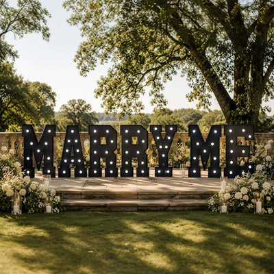 Outdoor wedding “Marry Me” sign with floral arrangements and candles