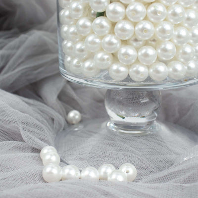 White decorative pearls in a glass jar with soft gray fabric backdrop.