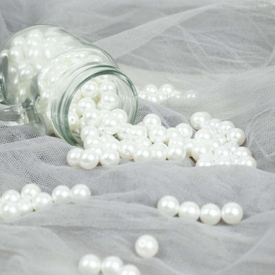 White decorative pearls spilling from a glass jar on soft gray fabric.