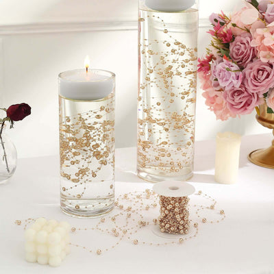 Decorative candles in elegant vases with floating gold beads and floral arrangement.
