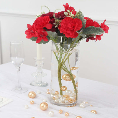 Red flower bouquet in a clear vase with decorative pearls on a table.