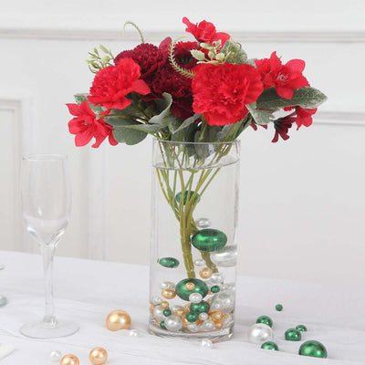 Red floral arrangement in a clear vase with decorative pearls and greenery.