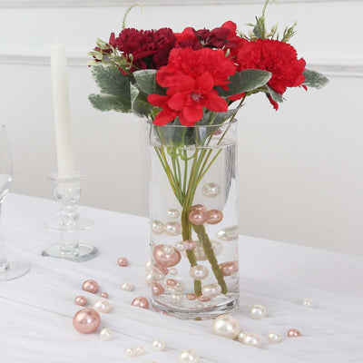Red flowers in a clear vase with decorative pearls on a table setting.