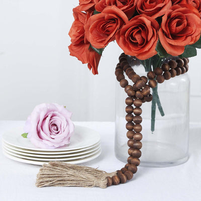 Decorative wooden beads with tassel beside a floral arrangement and plates.
