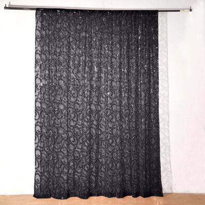 Black lace curtain hanging from a rod against a plain background.