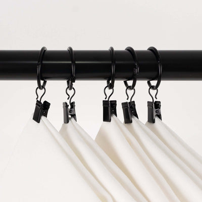 Black curtain clips holding white fabric on a rod