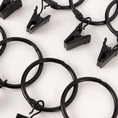 Black curtain clips on metal rings arranged in a pattern.