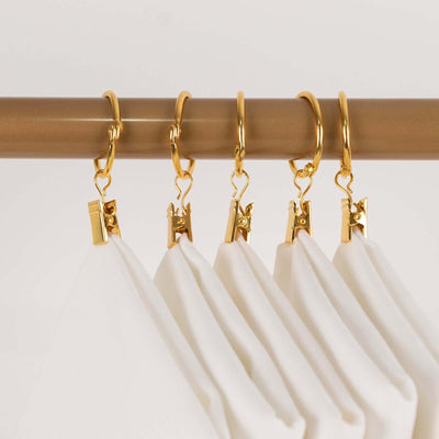 Gold curtain clips holding white fabric panels on a rod.