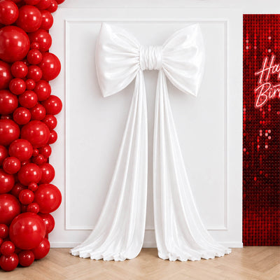 Red balloon wall with white draped bow decor and birthday backdrop