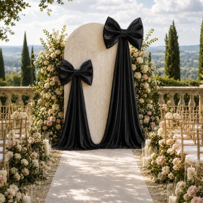 Elegant outdoor wedding aisle with black bows, floral arrangements, and arch backdrop