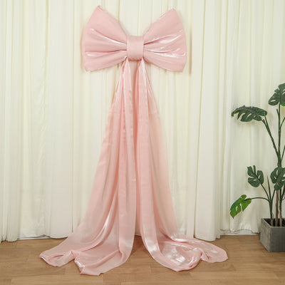 Large pink satin bow with flowing ribbons, ideal for event decor.