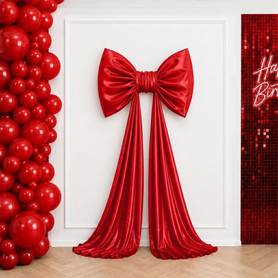 Red satin bow and draped backdrop with red balloon birthday party decor