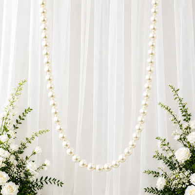 White pearl garland on sheer draped backdrop with elegant white floral arrangement