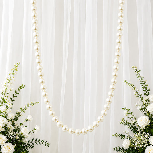 White pearl garland on sheer draped backdrop with elegant white floral arrangement