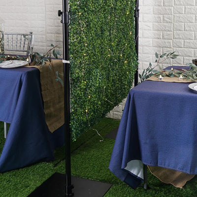 Decorative greenery backdrop for event tables with blue tablecloths.