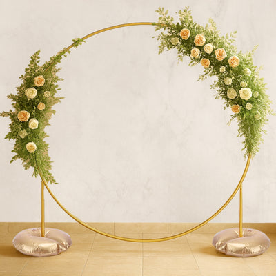 Gold circular floral arch with roses and greenery on a neutral background.