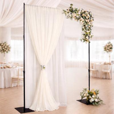 Elegant wedding backdrop with floral arch and draped fabric in reception setting.