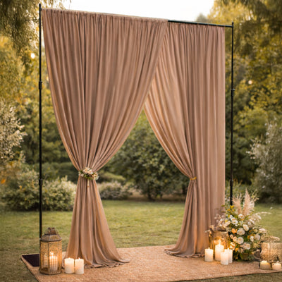Elegant outdoor wedding backdrop with draped fabric and decorative candles.