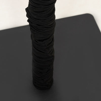 Black ruched fabric wrapped around a pole on a neutral background.