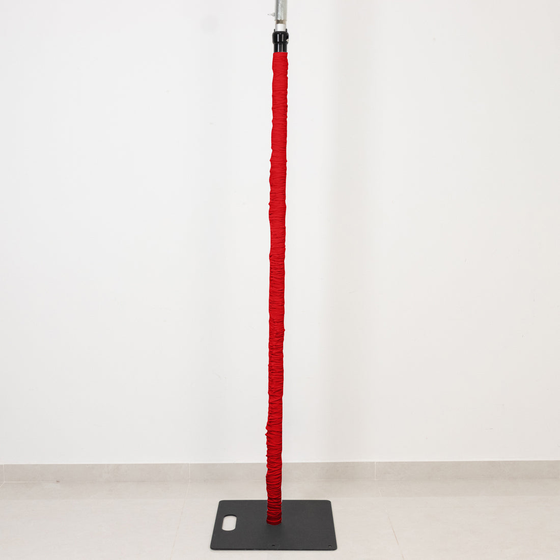 Red-wrapped vertical pole on black base against white wall